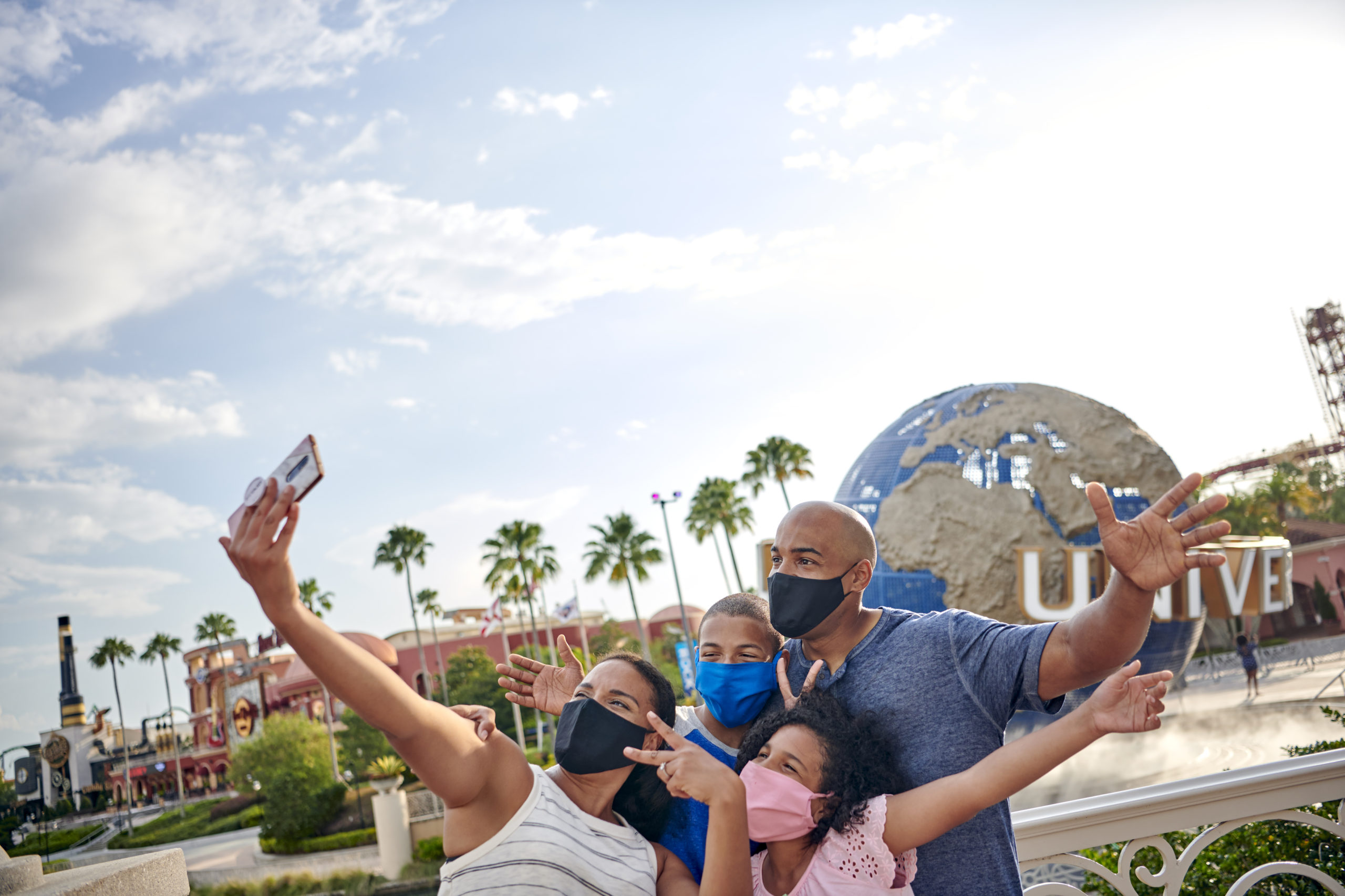 A mask-wearing family poses for a group selfie in front of the iconic Universal globe